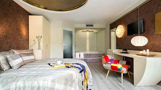 Ett modernt hotellrum med en dubbelsäng, färgglad stol och en jacuzzi i bakgrunden. (AI-genererad text)