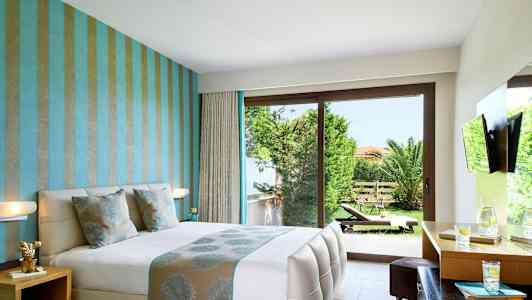 Ett hotellrum med en dubbelsäng, moderna möbler och utsikt över en grönskande trädgård genom stora glasdörrar. (AI-genererad text)