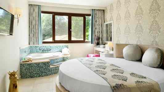 Ett hotellrum med en rund säng, jacuzzi vid ett fönster och klassisk inredning. (AI-genererad text)