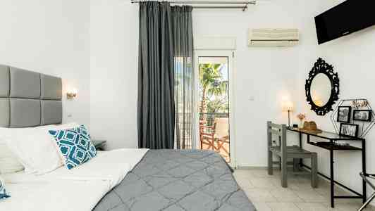 Ett hotellrum med en grå säng, ett skrivbord och en balkong med palmutiskt utsikt. (AI-genererad text)