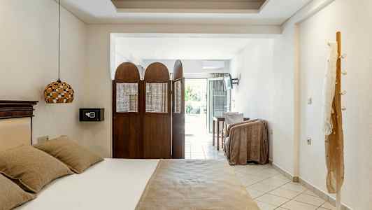 Ett hotellrum med en säng, skärmvägg, och ett bord framför en balkongdörr. (AI-genererad text)