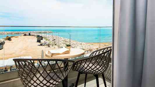 En balkong med två stolar och ett bord med en bok, utsikt över havet och en hamn. (AI-genererad text)