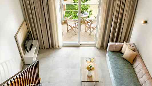 Utsikt över ett vardagsrum med en soffa, ett soffbord och en TV, med en balkong utanför glasdörrarna. (AI-genererad text)