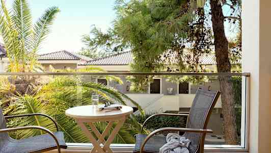 Utsikt från en balkong med bord, stolar och omgivande träd. (AI-genererad text)