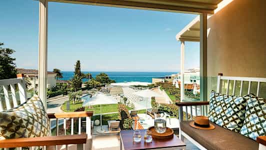 Vy från en terrass med sittmöbler mot en trädgård och havet. (AI-genererad text)