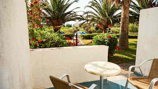 En uteplats med två stolar och ett bord, trädgård med palmer och blommor i bakgrunden. (AI-genererad text)