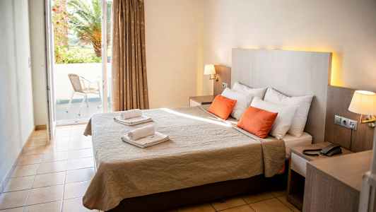 Bild av ett hotellrum med dubbelsäng, två röda kuddar och ett fönster som vetter mot en balkong. (AI-genererad text)