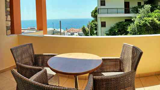 Balkong med bord och stolar samt utsikt över hav och byggnader. (AI-genererad text)