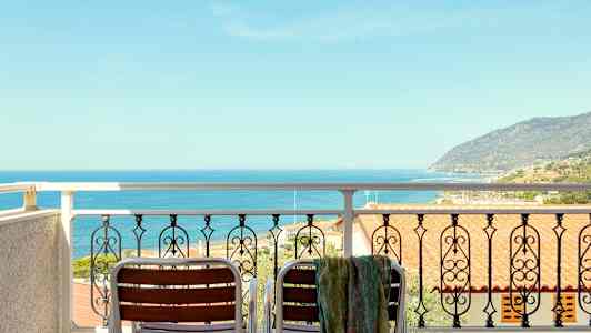 Utsikt från en balkong med två stolar och ett räcke mot havet och en kustlinje. (AI-genererad text)