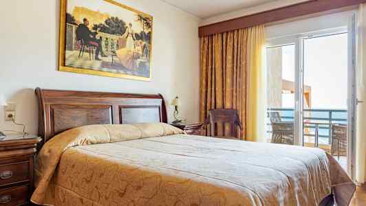 Ett hotellrum med en stor säng, trädetaljer och en balkong med havsutsikt. (AI-genererad text)