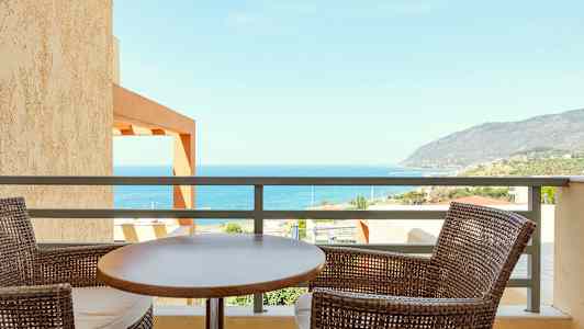 Utsikt över havet från en balkong, med två rottingstolar och ett bord i förgrunden. (AI-genererad text)