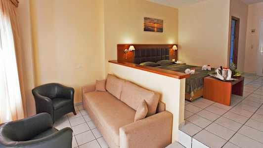 Ett hotellrum med en soffa, två fåtöljer och en säng bakom en låg skiljevägg. (AI-genererad text)