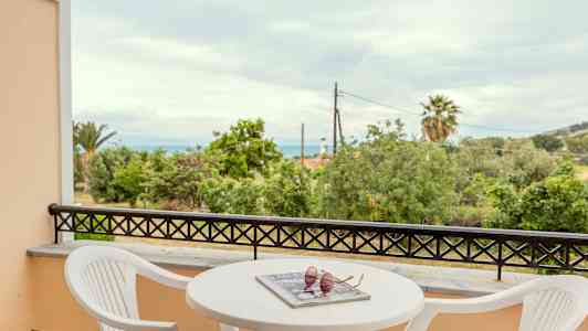 Balkong med utsikt över träd och hav, med bord och stolar. (AI-genererad text)