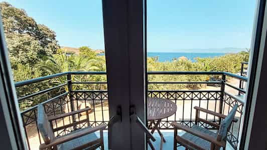 Utsikt från en balkong med två stolar och ett bord, havet och träd syns i bakgrunden. (AI-genererad text)