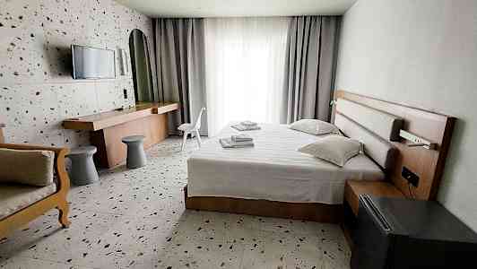 Ett hotellrum med säng, skrivbord och stol, samt ljusa gardiner vid fönstret. (AI-genererad text)