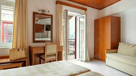 Ett hotellrum med två sängar, en spegel över ett skrivbord och en stol, samt en öppen balkongdörr med utsikt. (AI-genererad text)