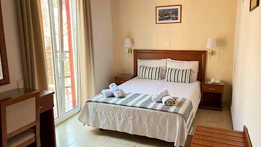 Ett hotellrum med en bäddad dubbelsäng, fönster med ljusa gardiner och möbler i trä. (AI-genererad text)