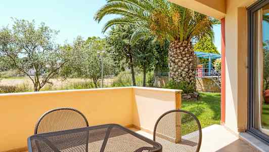 Balkong med bord och stolar samt utsikt över en trädgård med palmer. (AI-genererad text)