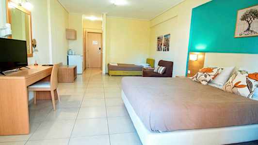 Ett hotellrum med en säng, soffa, skrivbord och TV, samt en dörr till en annan del av rummet. (AI-genererad text)