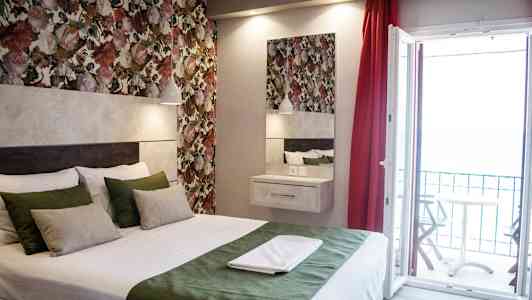 Ett rum med en säng, färgglada blomväggar och en öppen balkongdörr. (AI-genererad text)