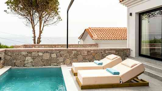 Utomhuspool med två solstolar och en utsikt över havet och hustakar. (AI-genererad text)