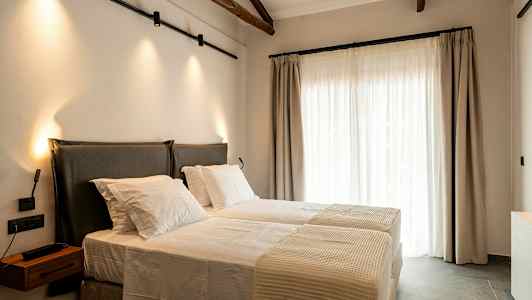 Ett sovrum med två bäddar, upplyst av vägglampor, med stora fönster täckta med ljusa gardiner. (AI-genererad text)