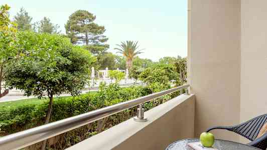 En balkong med utsikt över träd och en pool, med ett bord och en stol i förgrunden. (AI-genererad text)