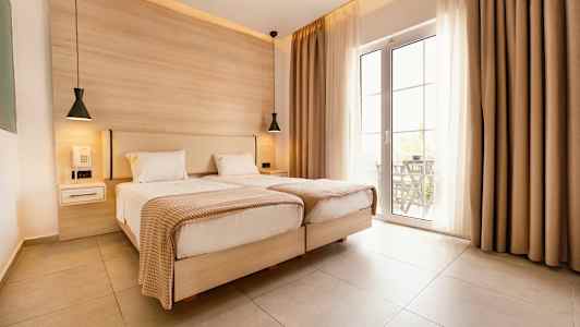 Två enkelsängar i ett ljust rum med stora glasdörrar och beige gardiner. (AI-genererad text)