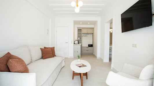 Vardagsrum med soffa, fåtölj, soffbord, TV och ett mindre kök. (AI-genererad text)