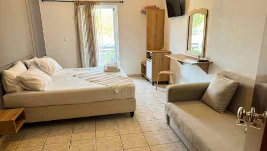 Ett hotellrum med en säng, soffa, skrivbord och garderob. Fönstret har ljusa gardiner. (AI-genererad text)