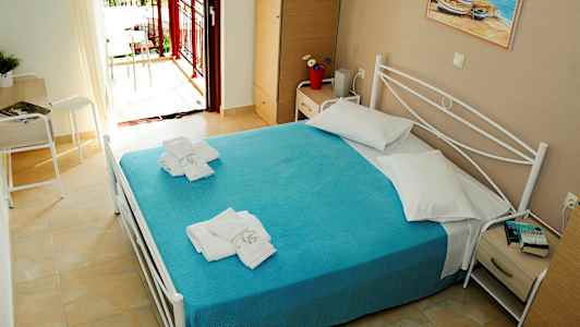 Ett hotellrum med en dubbelsäng bäddad med ett blått överkast och vita kuddar. På sängen ligger vikta handdukar. Rummet har en balkong med utsikt. (AI-genererad text)