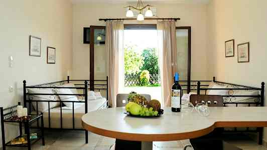 En inomhusmiljö med ett bord med frukt och en vinflaska, två bäddar och en öppen dörr som leder till en trädgård. (AI-genererad text)