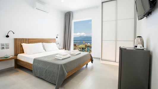 Modernt hotellrum med dubbelsäng, minikylskåp och utsikt över havet. (AI-genererad text)