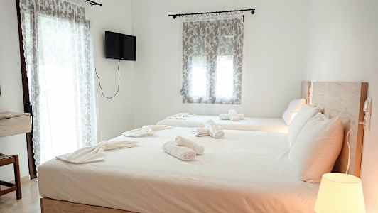 En hotellrum med två sängar, uppsatta med vita sängkläder och handdukar. En lampa på ett nattduksbord och en väggmonterad TV syns i rummet. (AI-genererad text)