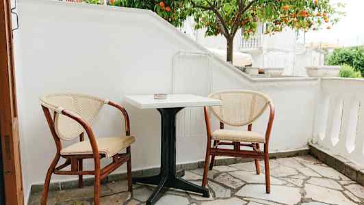 En liten uteplats med två stolar och ett bord framför ett apelsinträd. (AI-genererad text)