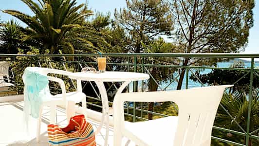 Utemöbler på en balkong med utsikt mot träd och vatten. (AI-genererad text)