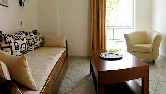 Ett vardagsrum med en soffa med geometriska mönster, ett runt bord och en ljus fåtölj vid ett fönster. (AI-genererad text)