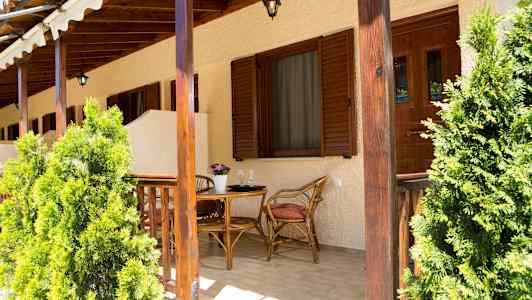 En uteplats med träbord och stolar, omgiven av gröna växter. (AI-genererad text)