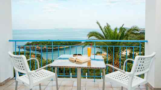Utsikt från en balkong mot havet, med ett bord och två stolar i förgrunden. (AI-genererad text)