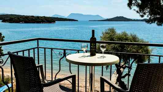 Två stolar och ett bord med ett vinflaska och glas på en balkong med utsikt över havet. (AI-genererad text)