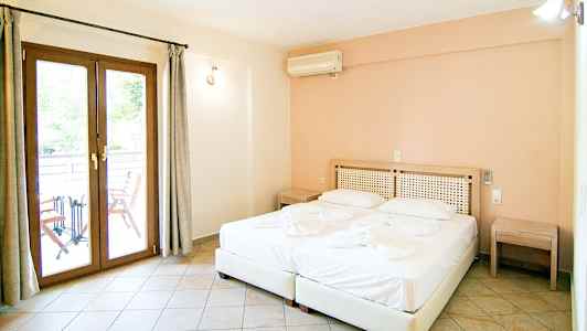 Ett hotellrum med en dubbelsäng, två nattduksbord, och en dörr till en balkong. (AI-genererad text)