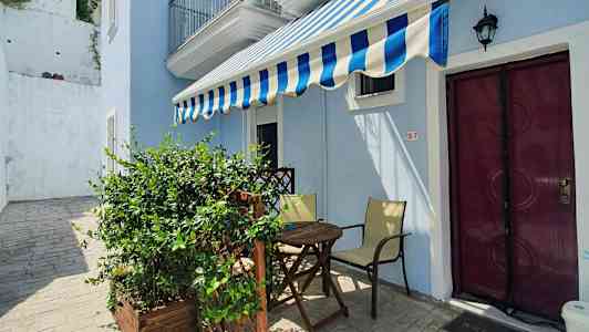 En liten uteplats med ett bord, stolar och en markis framför en ljusblå byggnad. (AI-genererad text)