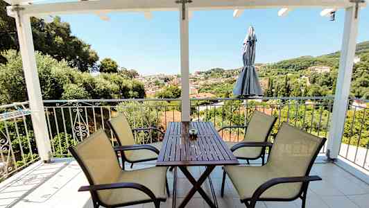 Uteplats med bord och stolar, utsikt över grönskande landskap och byggnader. (AI-genererad text)