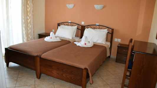 Två enkelsängar med vita sängkläder och dekoration, placerade i ett rum med terrakottamotstånd och mörka trämöbler. (AI-genererad text)