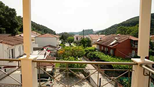 Vy från en balkong över hus med tegeltak och grönska samt berg i bakgrunden. (AI-genererad text)