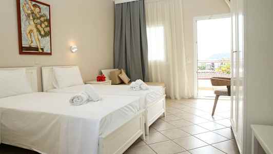 Ett hotellrum med två enkelsängar, vita lakan och handdukar. På väggen sitter en målning. Rummet har ett fönster och en balkongdörr. (AI-genererad text)