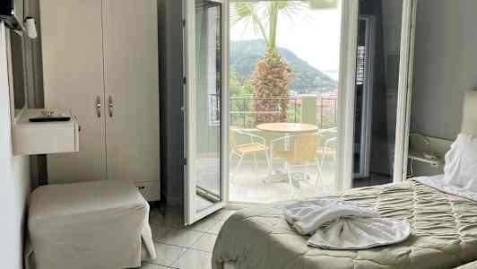 Hotellrum med utsikt mot en terrass med bord, stolar och en palm. (AI-genererad text)