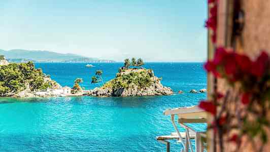 En liten ö med träd och ett hus omgiven av blått vatten. (AI-genererad text)