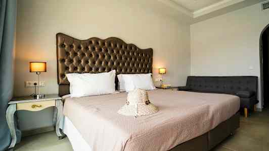 Ett hotellrum med en dubbelsäng, en soffa och nattduksbord med lampor, samt en hatt placerad på sängen. (AI-genererad text)