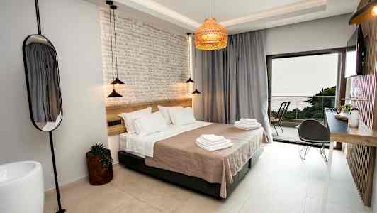 Ett modernt hotellrum med en stor säng, ljusa väggar och en dörr som öppnar sig mot en balkong med havsutsikt. (AI-genererad text)